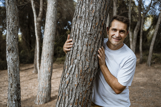 Smiling man embracing tree trunk in forest during vacation