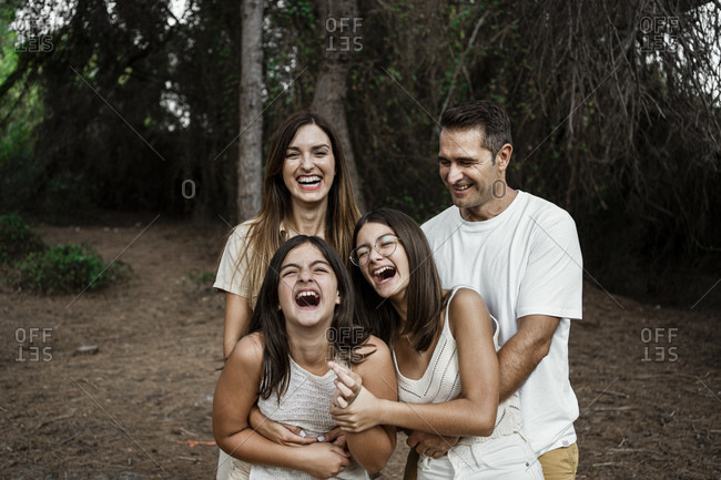 Parents with daughters laughing while standing in forest during vacation