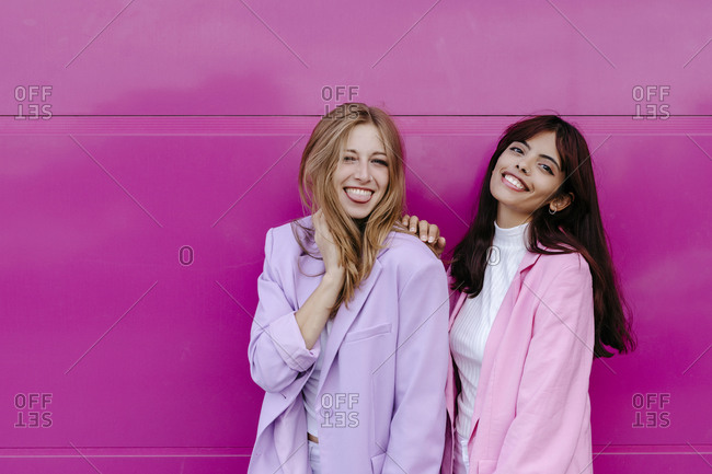 Happy siblings standing against pink wall