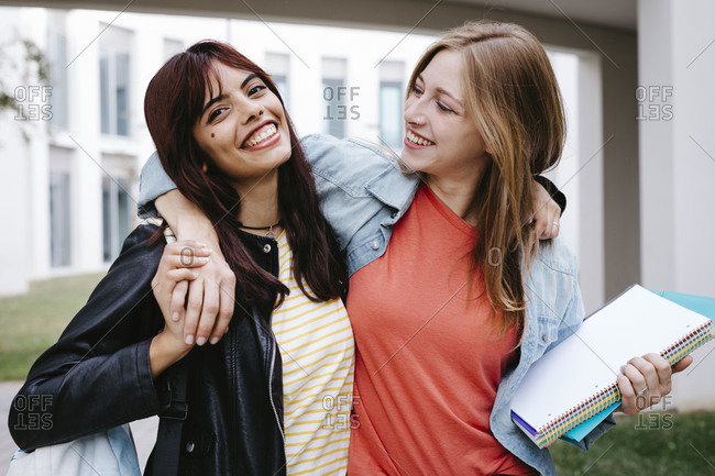 Smiling young student with arm around looking at friend in campus