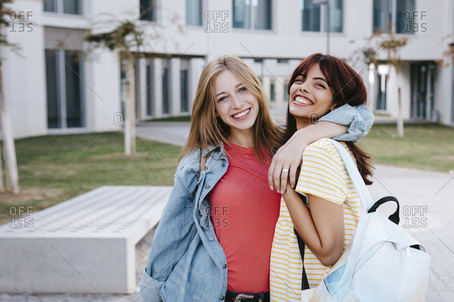 Cheerful young woman with arm around female friend at university campus