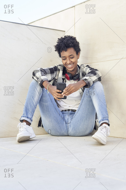 Smiling beautiful Afro woman using smart phone against retaining wall