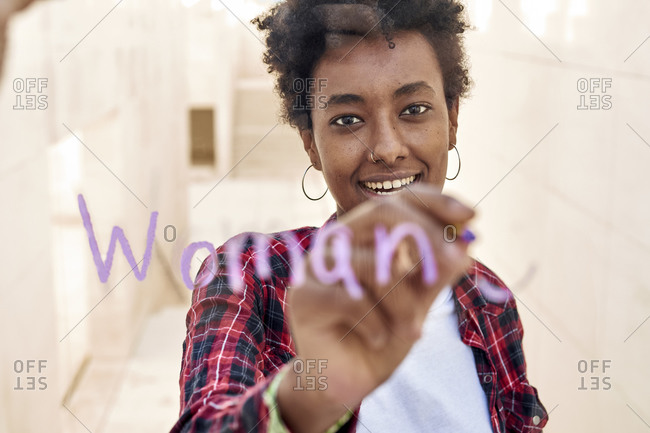 Smiling young female hipster writing WOMAN while celebrating Women's Day