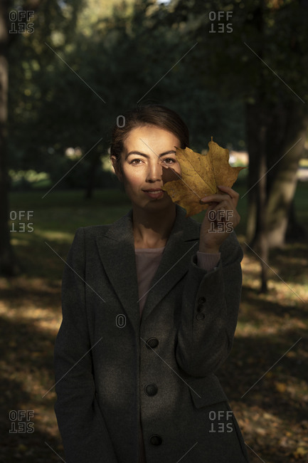 Female entrepreneur holding dry leaf while standing in park during autumn
