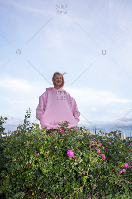 Young woman with pink hair wearing pink hooded shirt near rose bush
