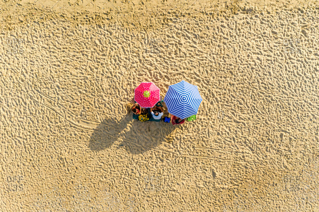 Aerial view of two umbrellas on the beach and people seating on their towels on Playa de Cuesta Maneli near Huelva, Spain.