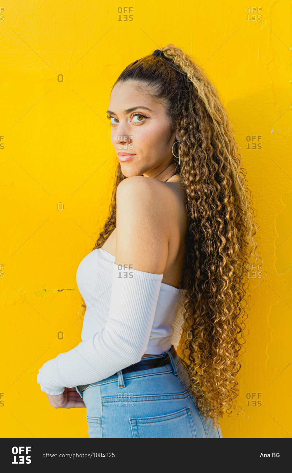 Portrait Of A Beautiful Latin Woman With Curly Hair Leaning On A Yellow