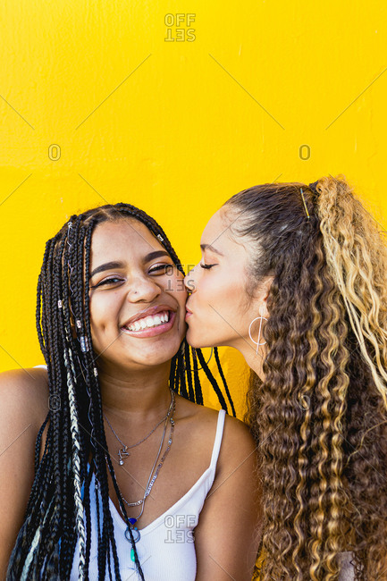 Portrait of a beautiful Latin woman kissing a black woman with braids with a yellow background