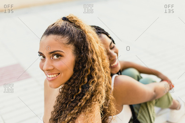 Portrait of a beautiful Latin woman looking at the camera leaning on the back of a black woman in the street