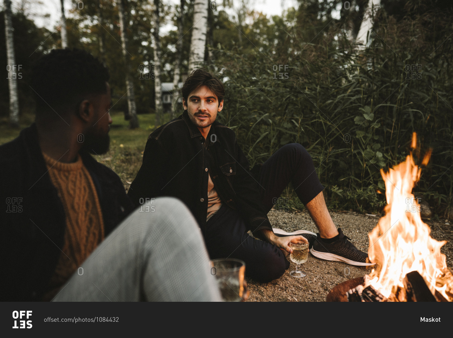 Male friends talking while sitting by fire pit during weekend