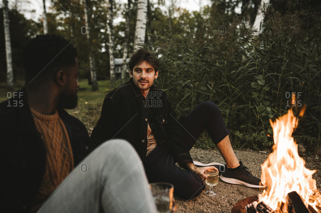 Male friends talking while sitting by fire pit during weekend