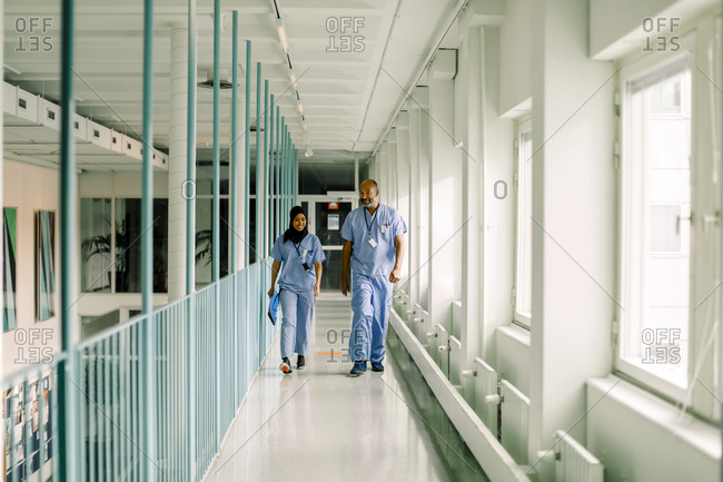 Male and female coworkers talking while walking in corridor at hospital