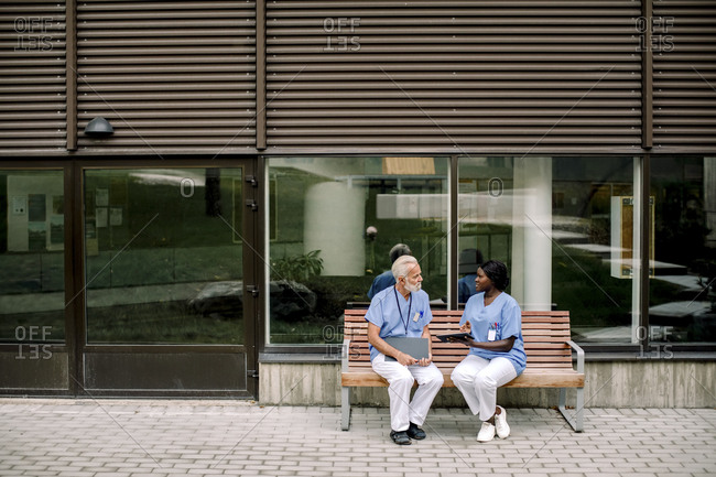Senior nurse talking to female colleague while sitting on bench