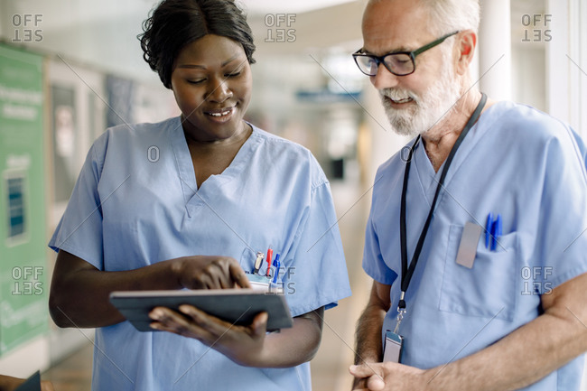 Smiling female nurse showing digital tablet to senior colleague in hospital