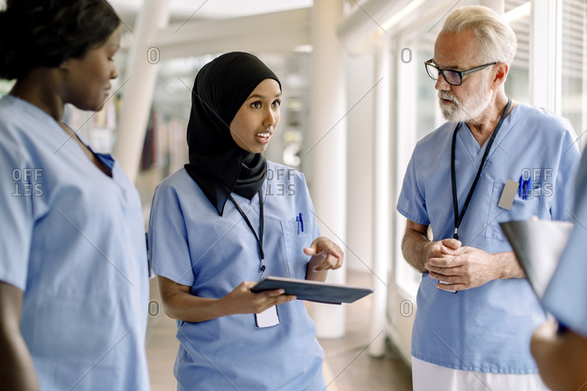 Confident female nurse with digital tablet talking to coworkers in hospital