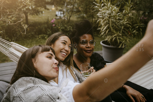 Smiling woman taking selfie with female friends through mobile phone during social gathering
