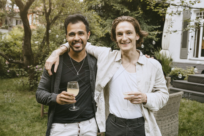 Portrait of man drinking while standing with male friend in yard
