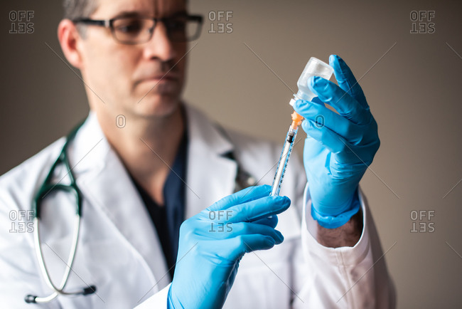 Doctor in white coat drawing vaccine into a syringe for injection.