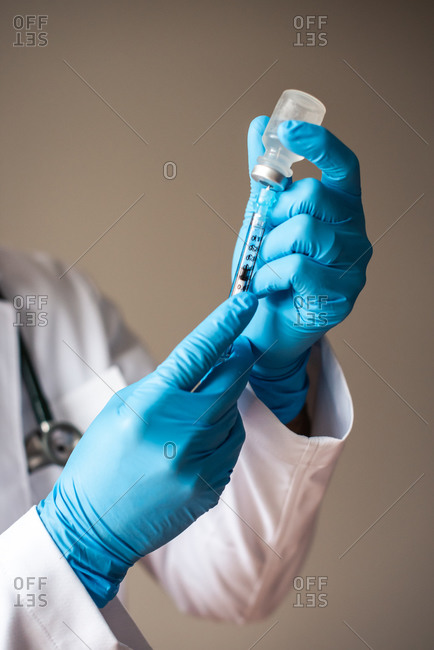 Doctor in white coat and gloves drawing vaccine into a syringe.