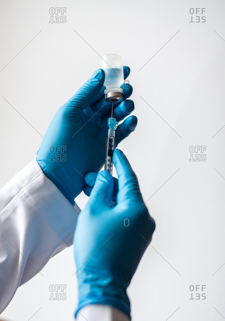 Hands in gloves drawing vaccine into syringe on white background.
