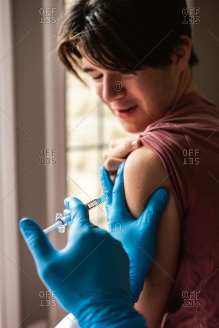 Close up of teen boy getting vaccinated by doctor holding a needle.