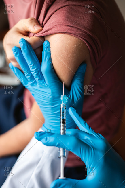Close up of teenager getting vaccinated by doctor holding a needle.