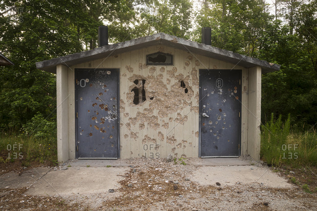 Campground bathroom pit toilet which has been riddled with bullets