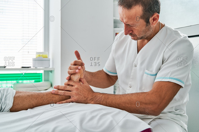 Concentrated male therapist massaging feet of patient lying on medical table in clinic during osteopathy session