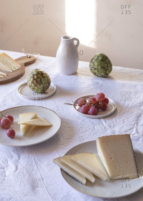 High angle of various palatable cheese arranged on table with Anona fruits and grapes near ceramic jug