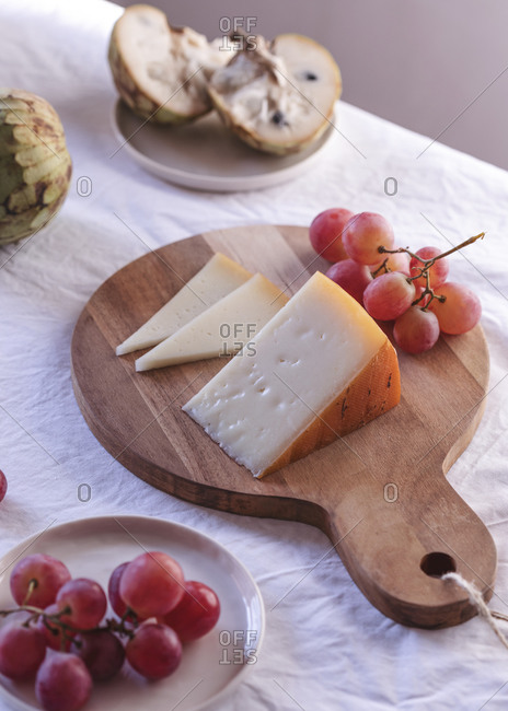 Table with sweet fruits and delectable cheese in bright room lit by sunlight