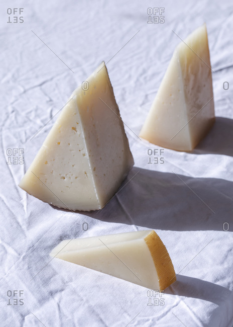 Assorted delicious pieces of fresh cheese arranged on white tablecloth in room lit by sunlight