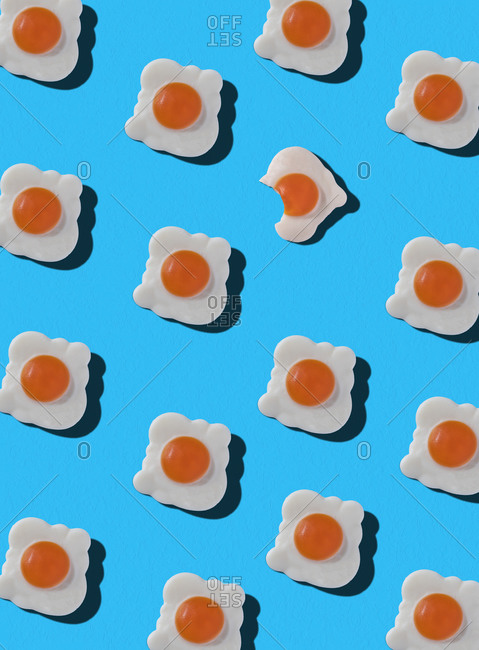 Top view of pattern of whole sweet candies in shape of fried eggs with one bitten arranged on blue background