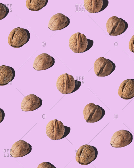 From above of brown walnuts arranged in rows on pink background in studio