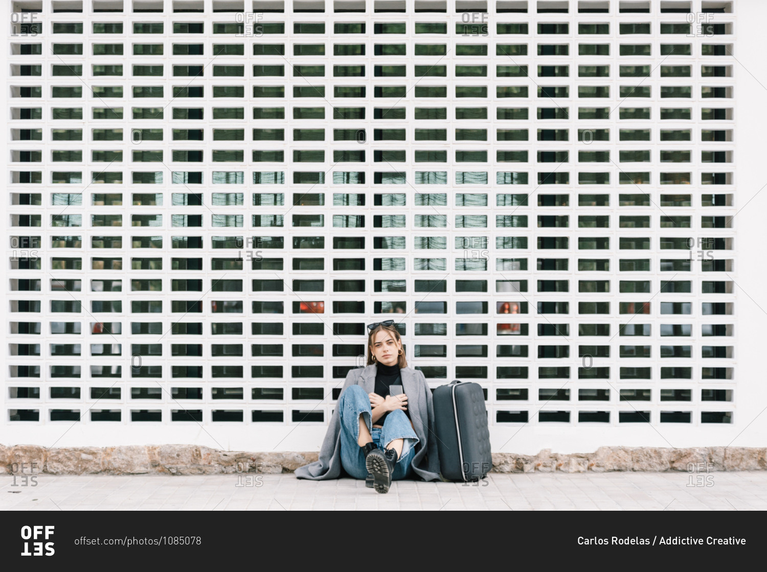 Female tourist with luggage sitting alone on pavement while getting lost in city looking at camera