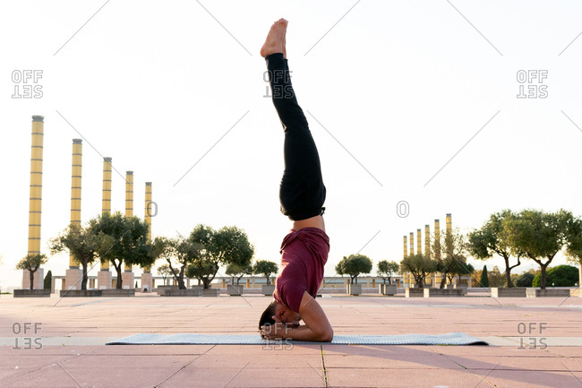 Side view of male in sportswear balancing on arms in Handstand asana while practicing yoga on mat in urban park on sunny day