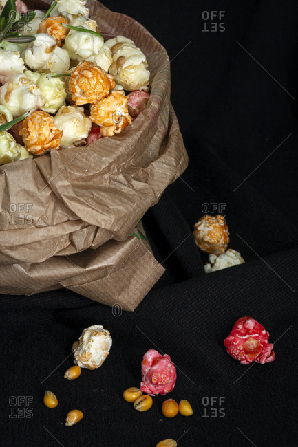 High angle of heap of varicolored sweet popcorn in paper bag placed with yellow corn seeds on black background in studio