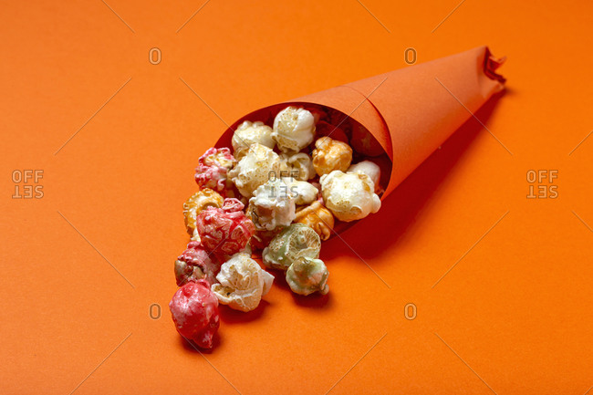High angle of colorful tasty popcorn in paper cone placed on orange background in studio