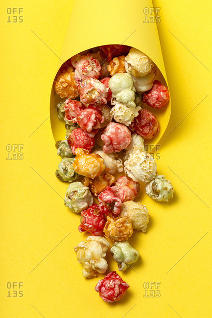 High angle of colorful tasty popcorn in paper cone placed on yellow background in studio