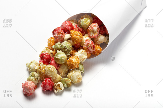High angle of colorful tasty popcorn in paper cone placed on white background in studio
