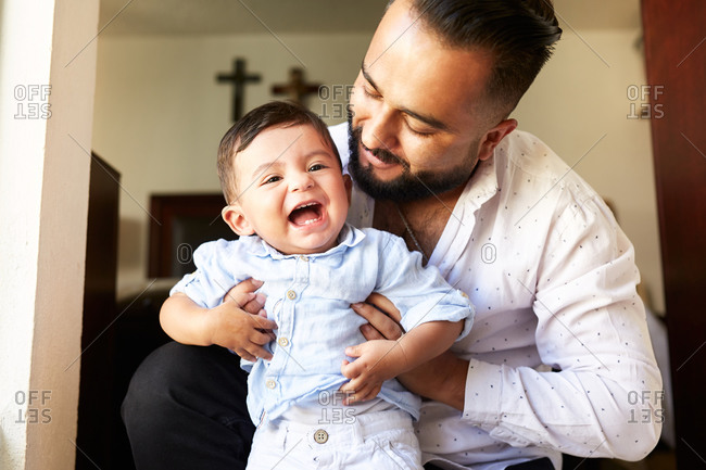Delighted Hispanic father having fun with adorable little kid while spending time together at home