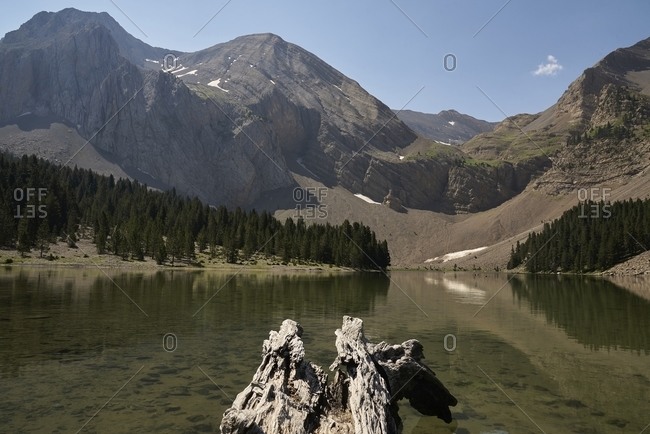 Scenery of calm pond with clean water near mountains under blue cloudless sky on sunny day