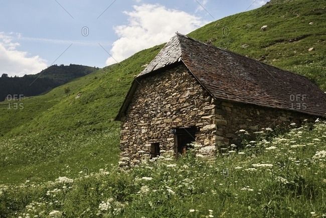 Low angle of aged stone hut on green slope in highlands on summer day in Barrosa cirque