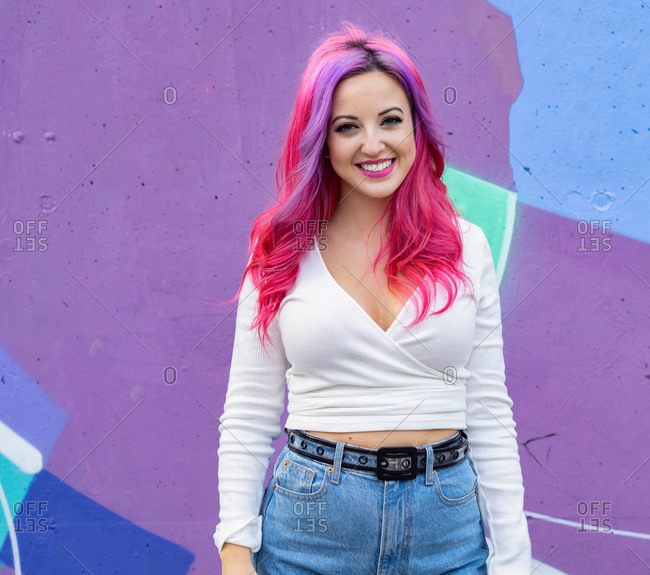 Modern millennial hipster female with dyed long hair looking at camera while standing against bright colorful wall