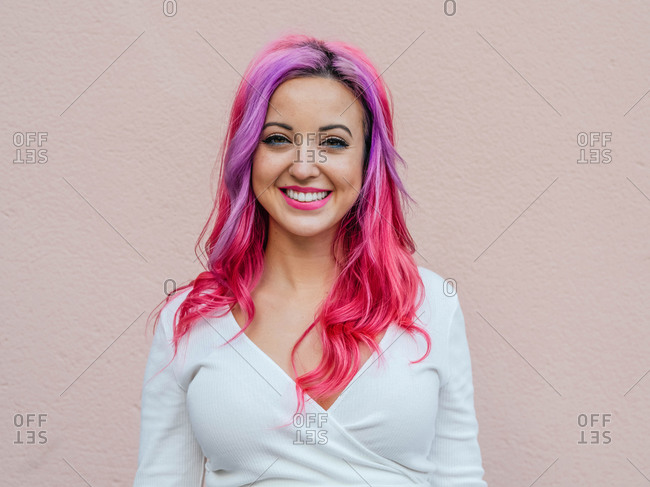 Modern millennial hipster female with dyed long hair looking at camera while standing against beige background