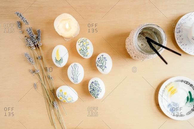 Top view of chicken eggs painted with aquarelle placed on table with lavender flowers and burning candle for Easter