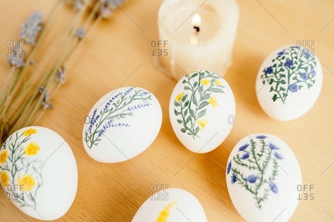 Top view of chicken eggs painted with aquarelle placed on table with lavender flowers and burning candle for Easter