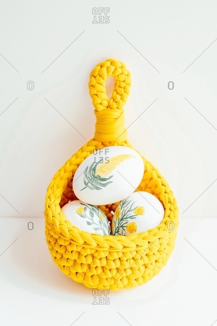 Handmade crochet basket with white chicken eggs painted with flowers placed on wooden table for Easter