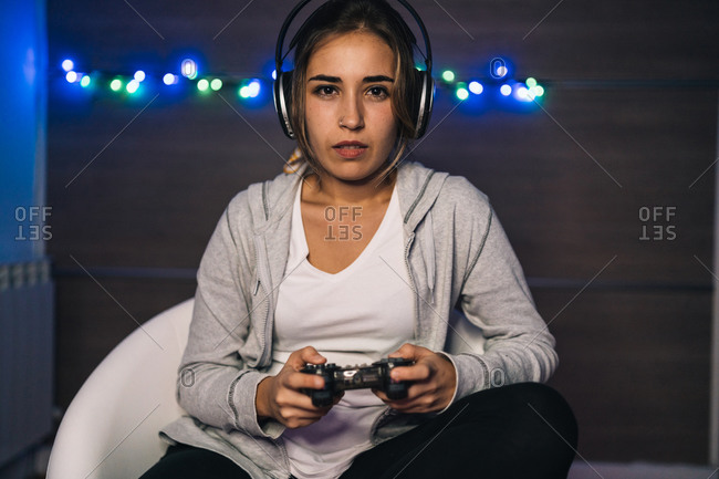 Concentrated female in headphones and with console sitting in armchair and playing video game while entertaining in evening at home