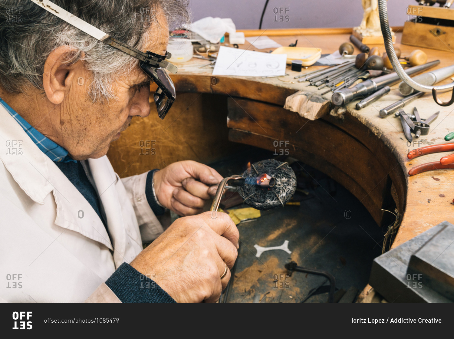 High angle side view of skilled mature male master in glasses using soldering iron while working at workbench with professional instruments in jewelry workshop
