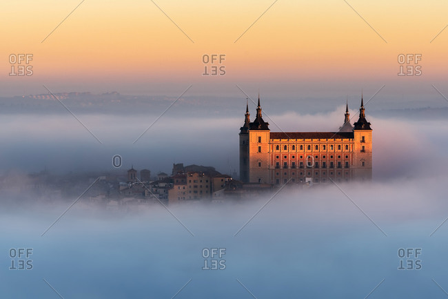 Drone view of peaks of old castles among dense clouds at colorful sunset with hills on horizon in Toledo